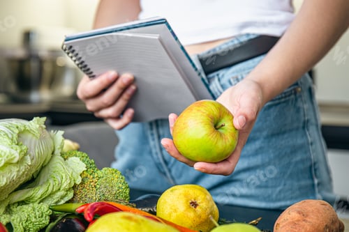 Preview: Woman with notepad and vegetables on the kitchen table preparing a recipe.