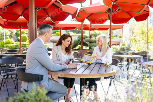Preview: Business people reviewing contract terms on a tablet at an outdoor cafe