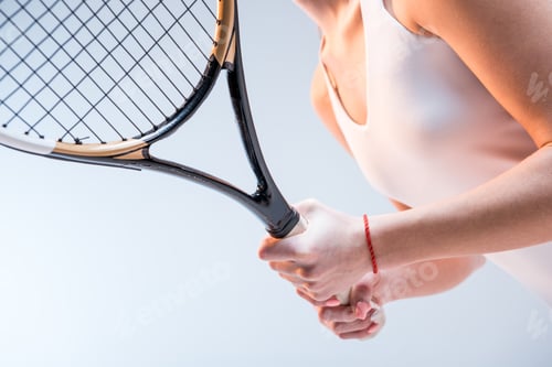 Preview: Close-up partial view of young woman in sportswear holding tennis racquet isolated on grey