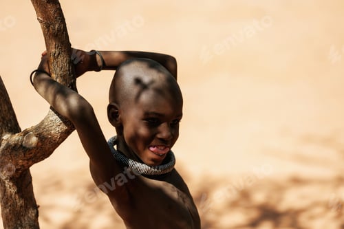 Preview: Namibia, Africa - June 14, 2021: Standing near tree. Child of the ethnic people of Africa