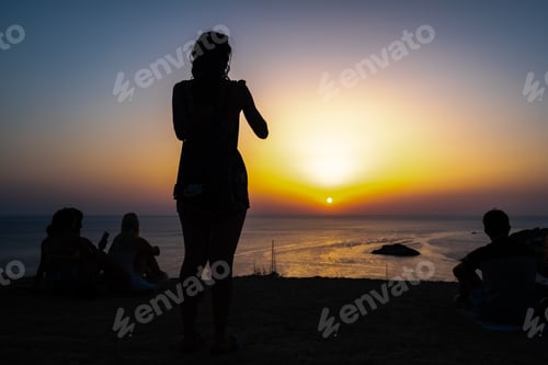 Preview: Woman enjoys the sunset on the shore of a paradisiacal beach during summer vacations.