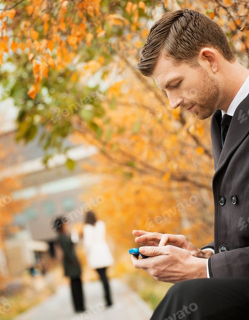 Preview: City life. A man in the park checking and texting, keeping in contact, using a mobile phone.