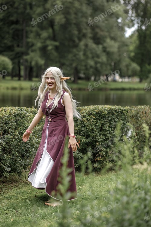 Preview: Young elf girl with blond long hair. Medieval elven princess in a burgundy dress in the forest