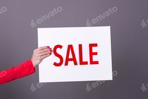 Preview: Female hand holding a Sale poster. Studio shot. Commercial concept.