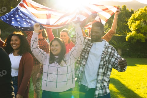 Preview: Happy diverse male and female friends holding american flag in sunny garden