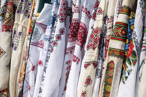 Preview: Display of traditional embroidered garments with intricate, colorful patterns hanging in a row.
