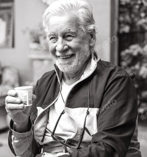 Preview: Black and white portrait of smiling senior bearded man sitting in cafeteria with espresso coffee cup
