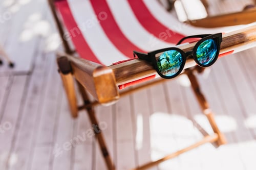 Preview: Sparkle female sunglasses lying on striped recliner. Photo of elegant summer glasses on chaise-long