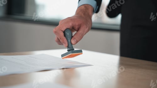 Preview: Businessman hand stamping an approved stamp on a text document at a table.