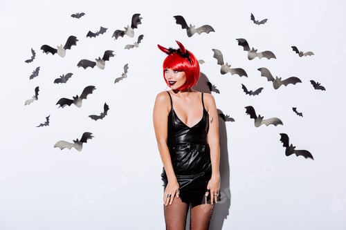 Preview: girl in devil Halloween costume near white wall with decorative bats