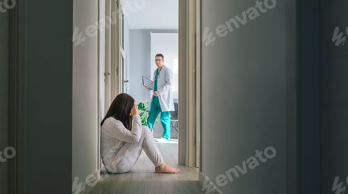 Preview: Doctor looking at female patient with mental disorder sitting on floor in hospital