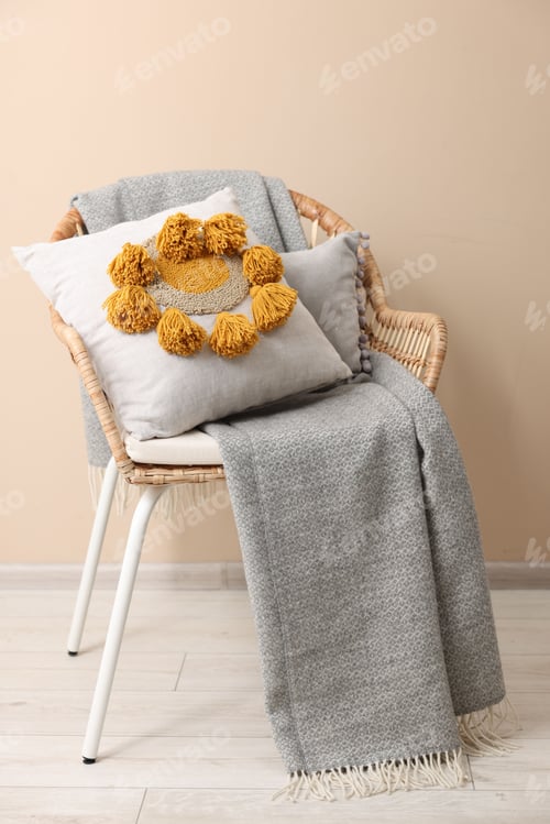 Preview: Stylish soft pillow and blanket on armchair near beige wall indoors