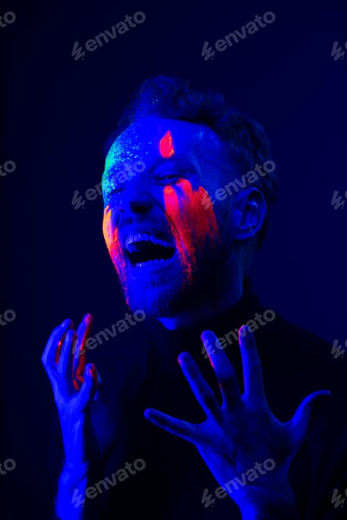 Preview: Fashion portrait. A man with fluorescent paint on his face under neon light.