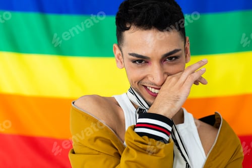 Preview: Portrait of happy biracial transgender man looking at camera with rainbow flag in background