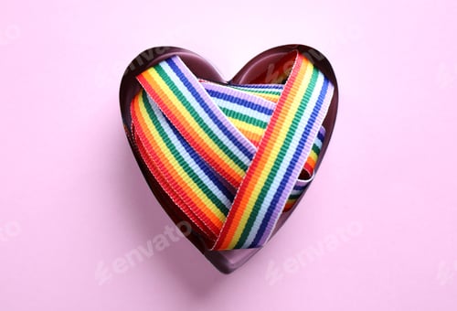 Preview: Heart shaped mold with bright rainbow ribbon on color background, top view. Symbol of gay community