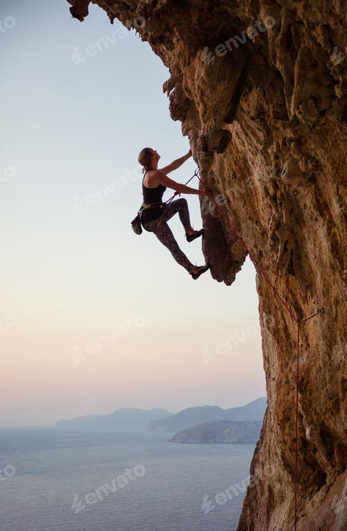 Preview: Young woman climbing challenging route at sunset