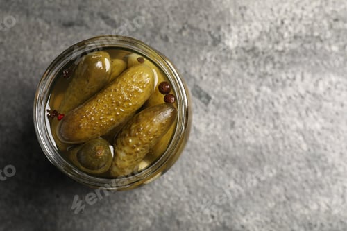 Preview: Tasty pickled cucumbers in glass jar on grey table, top view. Space for text