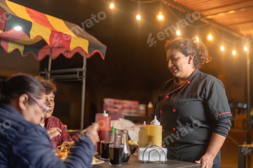 Preview: Female chef serving customers eating chicken at night street food stand