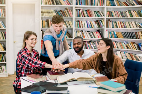 Preview: Group of young joyful multiracial college students collaborating on project, sitting at the table in