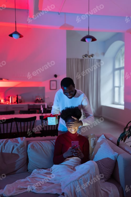 Preview: Loving african man husband congratulates happy excited wife, covers her eyes and give birthday gift