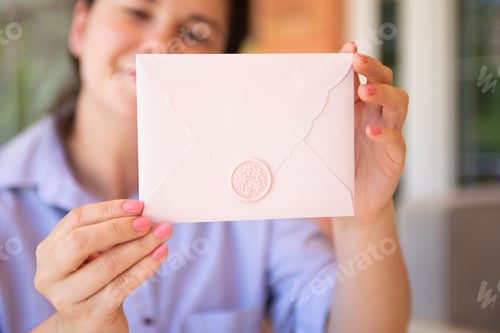 Preview: Closeup photography of defocused woman,holding pink invitation envelope with wax seal.