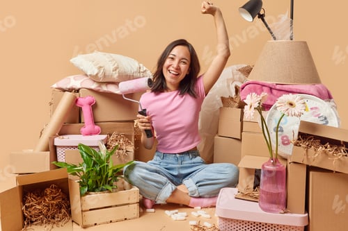 Preview: Happy Asian woman going to paint walls in room relocates to new apartment dressed casually sits in