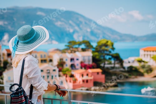 Preview: Tourist woman wearing blue sunhat and white clothes enjoying view of colorful tranquil village Assos