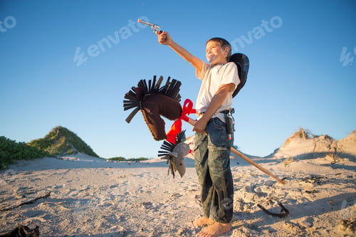 Preview: Boy dressed as cowboy with hobby horse in sand dunes
