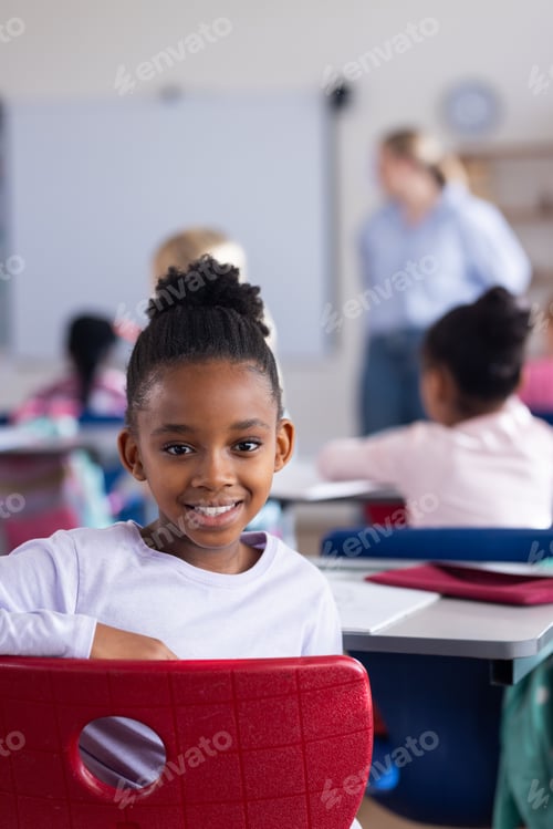 Preview: In school, african american girl smiling while sitting at desk in classroom, looking happy