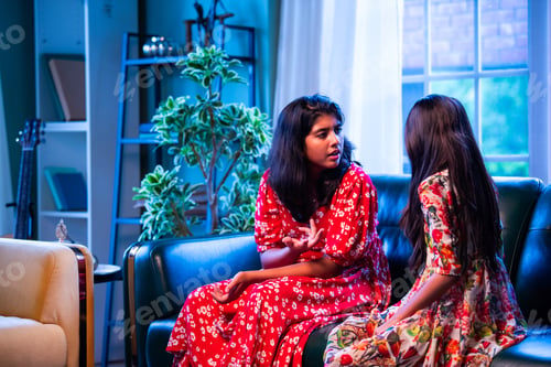 Preview: Two Indian sisters sit quietly on sofa, upset with each other, showing childhood emotions at home