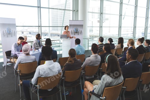 Preview: Businesswoman speaking in front of business people sitting at seminar in office building