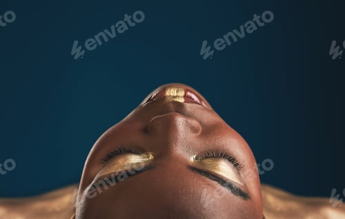 Preview: Beauty, gold makeup and art on face of black woman with creative gold aesthetics isolated in a stud