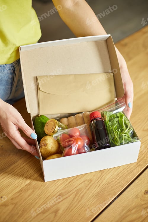 Preview: Woman put on the table food box meal kit of fresh ingredients order from a meal kit company