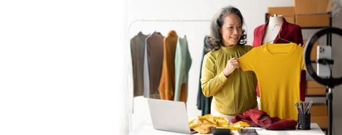Preview: Happy senior woman doing online clothes business, masuring, holding new beautiful shirt for her cust