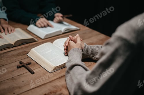 Preview: Group of Christians sit together and pray around a wooden table with blurred open Bible pages