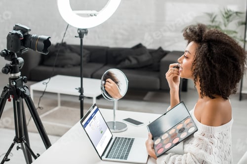 Preview: KYIV, UKRAINE - DECEMBER 10, 2019: side view of african american influencer holding eye shadow