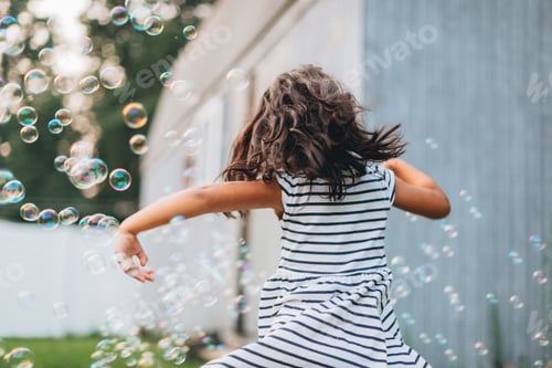 Preview: Diverse pre school girl at home dancing and having fun alongside bubbles being carefree and happy