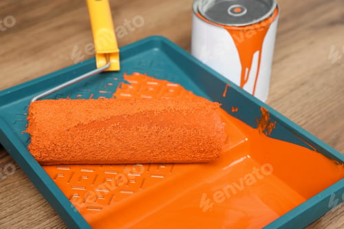 Preview: Can of orange paint, tray and roller on wooden table, closeup