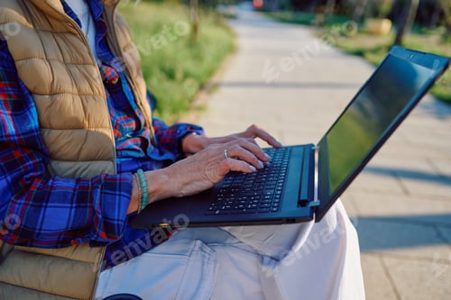 Preview: Senior person using a laptop outdoors on a sunny day
