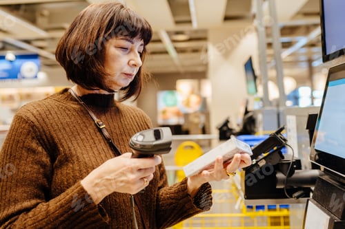 Preview: Senior woman scanning product with barcode reader in home goods store