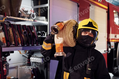 Preview: Holds hose. Male firefighter in protective uniform standing near truck
