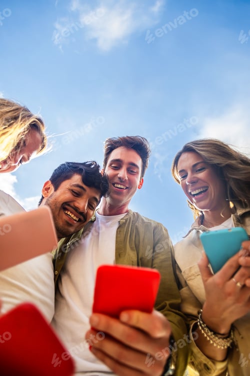 Preview: Young people using mobile phone device standing in circle outdoors