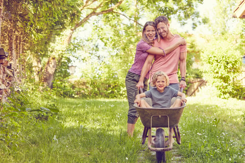 Preview: Family enjoying time in a sunny garden with a child in a wheelbarrow