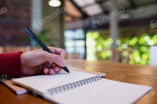 Preview: Closeup image of a woman writing on a notebook on the table