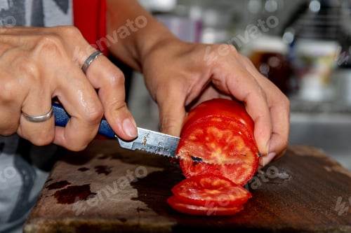Preview: Male slicing red fresh tomato using a small bread knife on a wooden chopping board