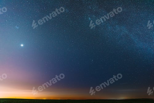 Preview: Night Starry Sky With Glowing Stars Above Countryside Field Landscape In Early Spring. Bright Glow