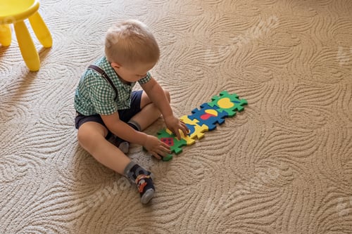 Preview: A little boy student sitting on the floor performs a task collecting puzzles at school at home.