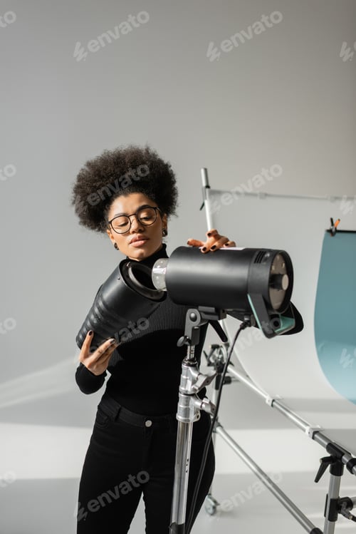 Preview: african american content producer in eyeglasses assembling strobe spotlight in photo studio