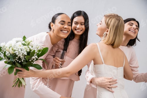Preview: wedding preparations, happy bride with bouquet hugging cheerful multicultural bridesmaids with
