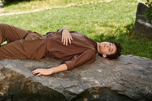 Preview: Young man relaxes on a rock in a sunny park, flaunting his summer style